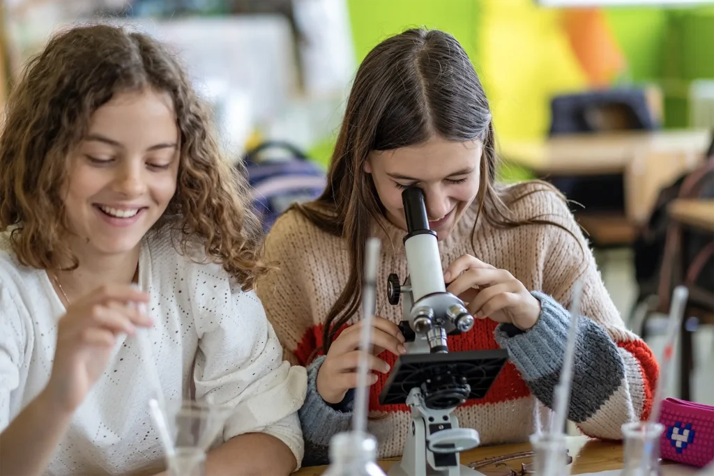 Teenagers students in a science classroom observing with a microscope